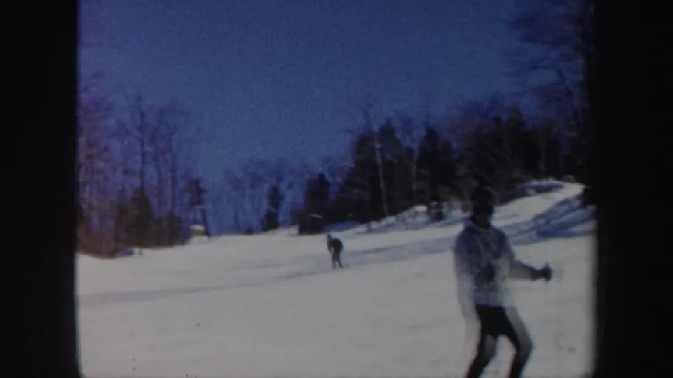 The skier passes near the frame edge on a wide snowy Vermont slope, with another skier visible in the distance.
