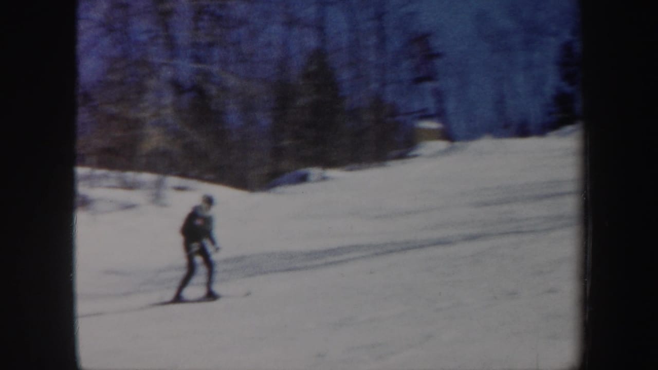 Skier gliding downhill with snowfield and lift structure in the background.