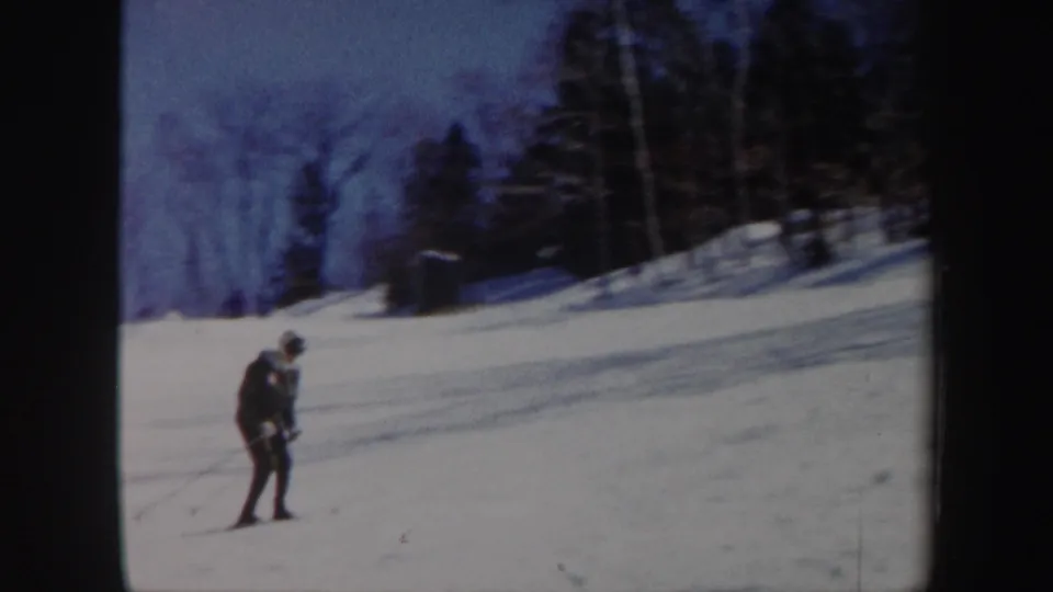 A skier in dark gear leans into the descent on a snow-covered Vermont trail in soft 8mm color.