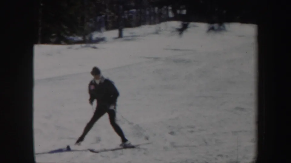 Adult skier crosses the snowy Vermont slope with poles, framed by dark woods in 1962 home-movie footage.