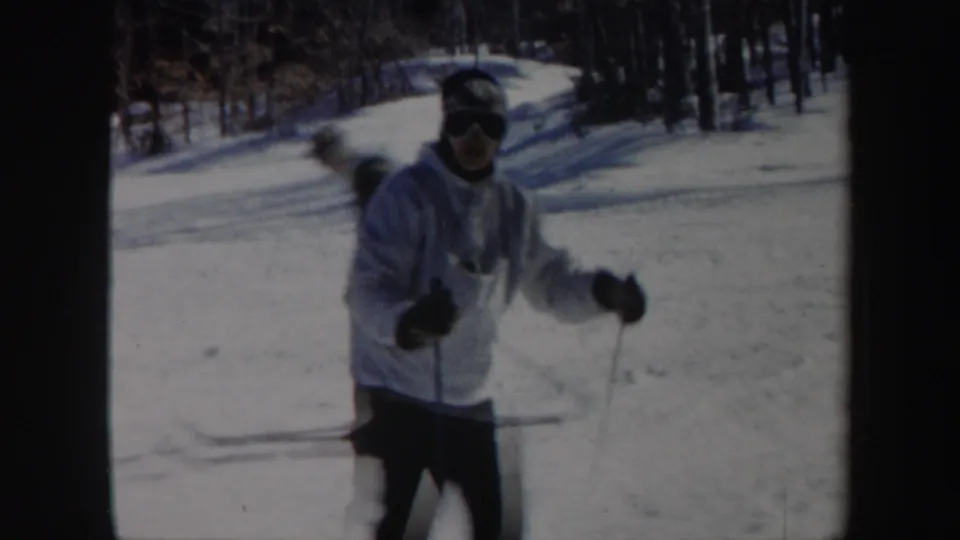 An adult skier wearing a light jacket and goggles approaches the camera during a snowy Vermont practice run.