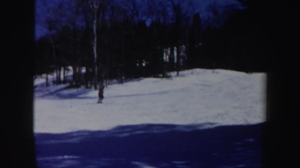 A distant skier moves through a snowy clearing in wooded Vermont, seen in grainy 8mm footage from 1962.