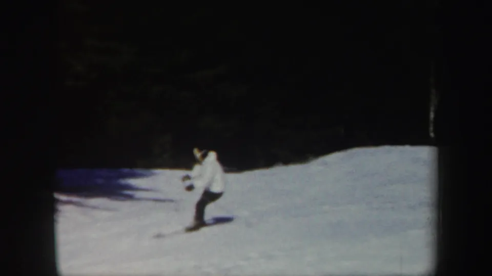 1962 Vermont 8mm frame showing a distant skier in a white jacket crossing a snow-covered slope near a dark tree line.