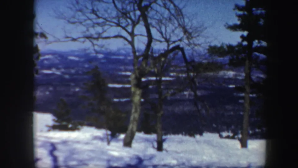 1962 Vermont 8mm view of a snowy hillside, bare trees, evergreens, and distant winter hills beneath a blue sky.