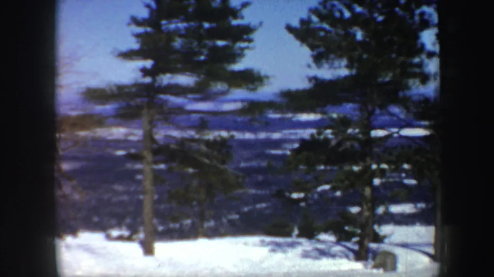 1962 Vermont 8mm frame showing snow-covered ground, evergreen trees, and distant wooded hills from a winter overlook.