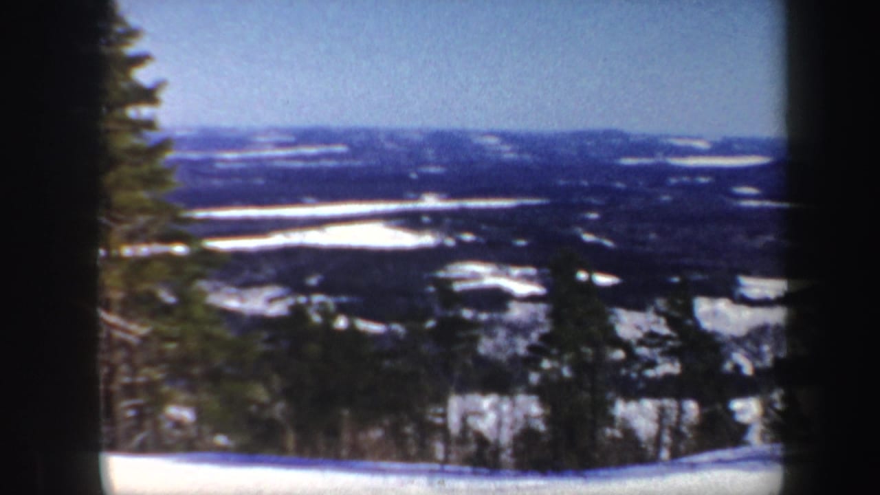 Snowy landscape with distant dark hills and trees under a blue sky.