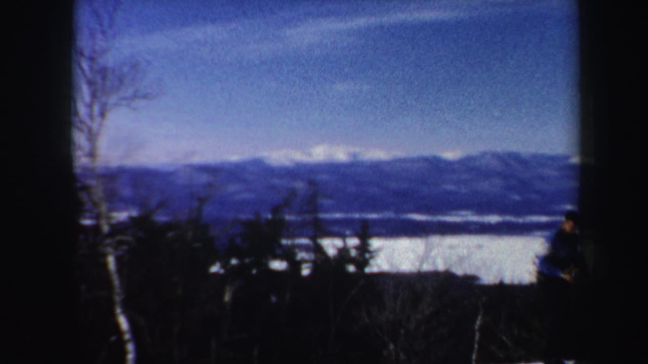 Vermont winter vista with lake, distant mountains, dark foreground trees, and a partially visible person at the frame edge.