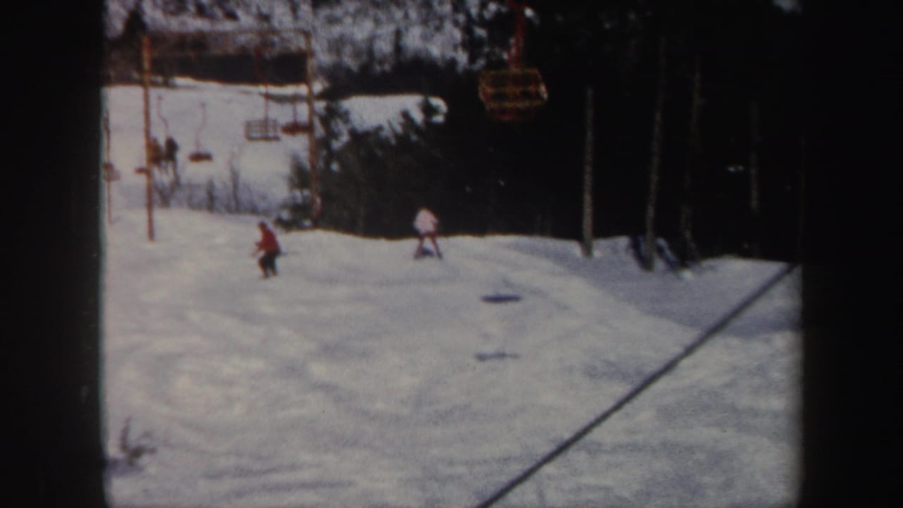 Several skiers appear on a snowy slope with lift chairs overhead.