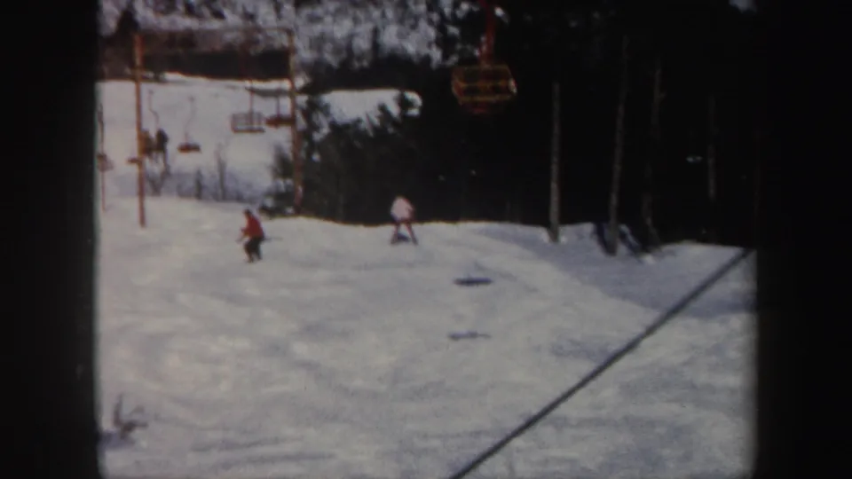 Wide 1962 Vermont ski-slope view with small figures on snow and lift chairs or cables above the hill.