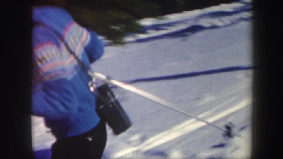 Close 8mm frame of a skier in a blue patterned sweater and dark pants moving across bright snow in Vermont.