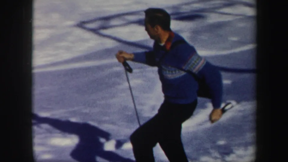 Man skiing past the camera in a blue patterned sweater on a snowy Vermont slope, with strong shadows across the snow.