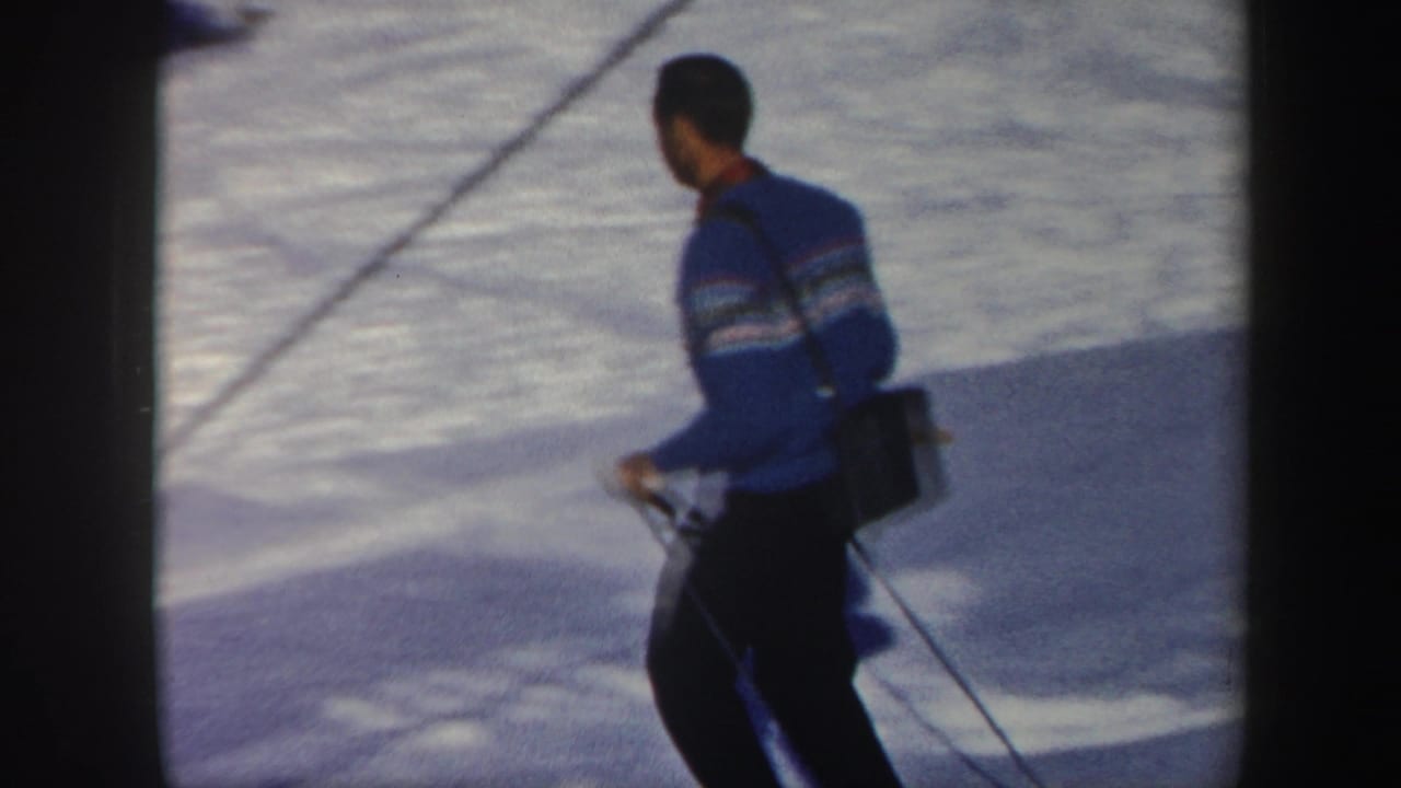 In supported 1962 Vermont home-movie footage, a man in a blue patterned sweater skis across bright snow with poles and a small pack.