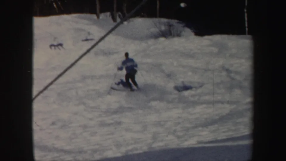 1962 Vermont home-movie frame showing a skier descending a snowy slope near lift cables and evergreen trees.
