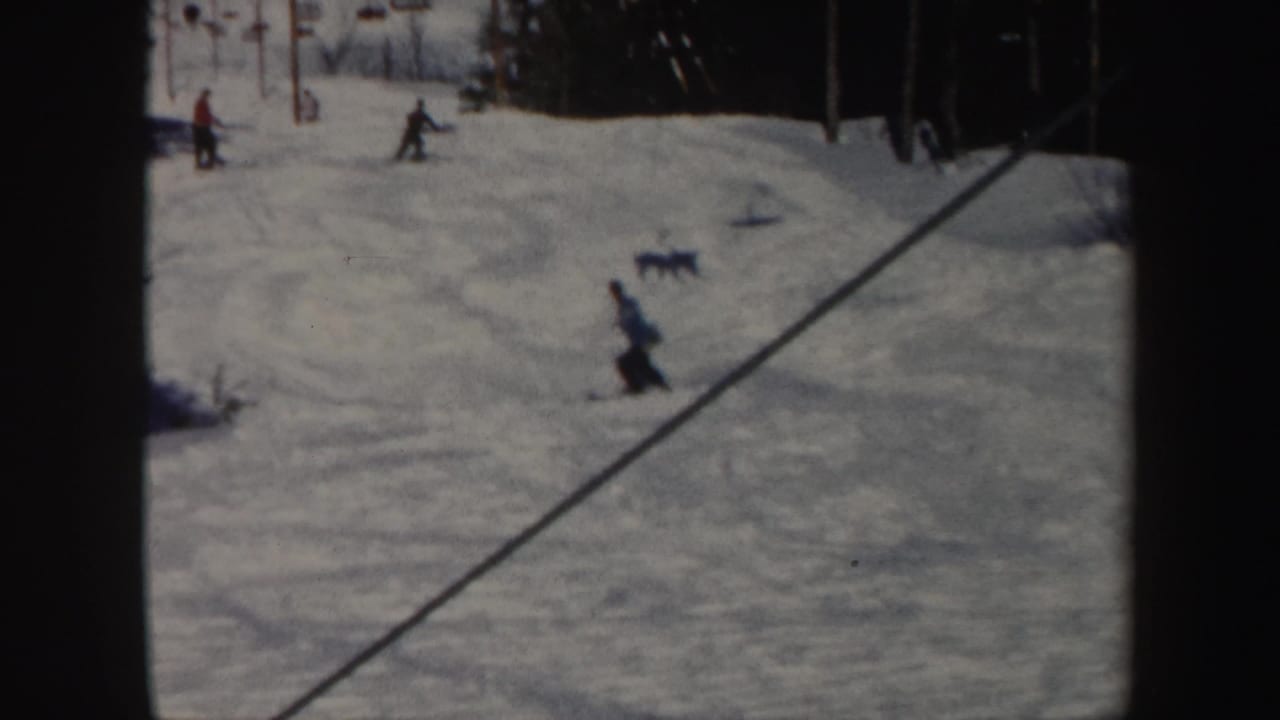 1962 Vermont ski-slope view with distant skiers, lift towers, evergreen trees, and textured snow.