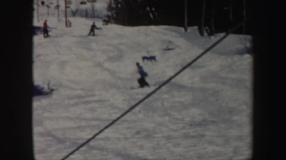 1962 Vermont ski-slope view with distant skiers, lift towers, evergreen trees, and textured snow.