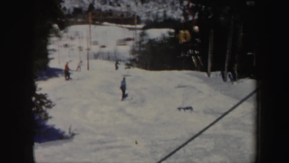 1962 Vermont frame showing a skier on the lower slope with other skiers, lift towers, cables, and trees in the background.