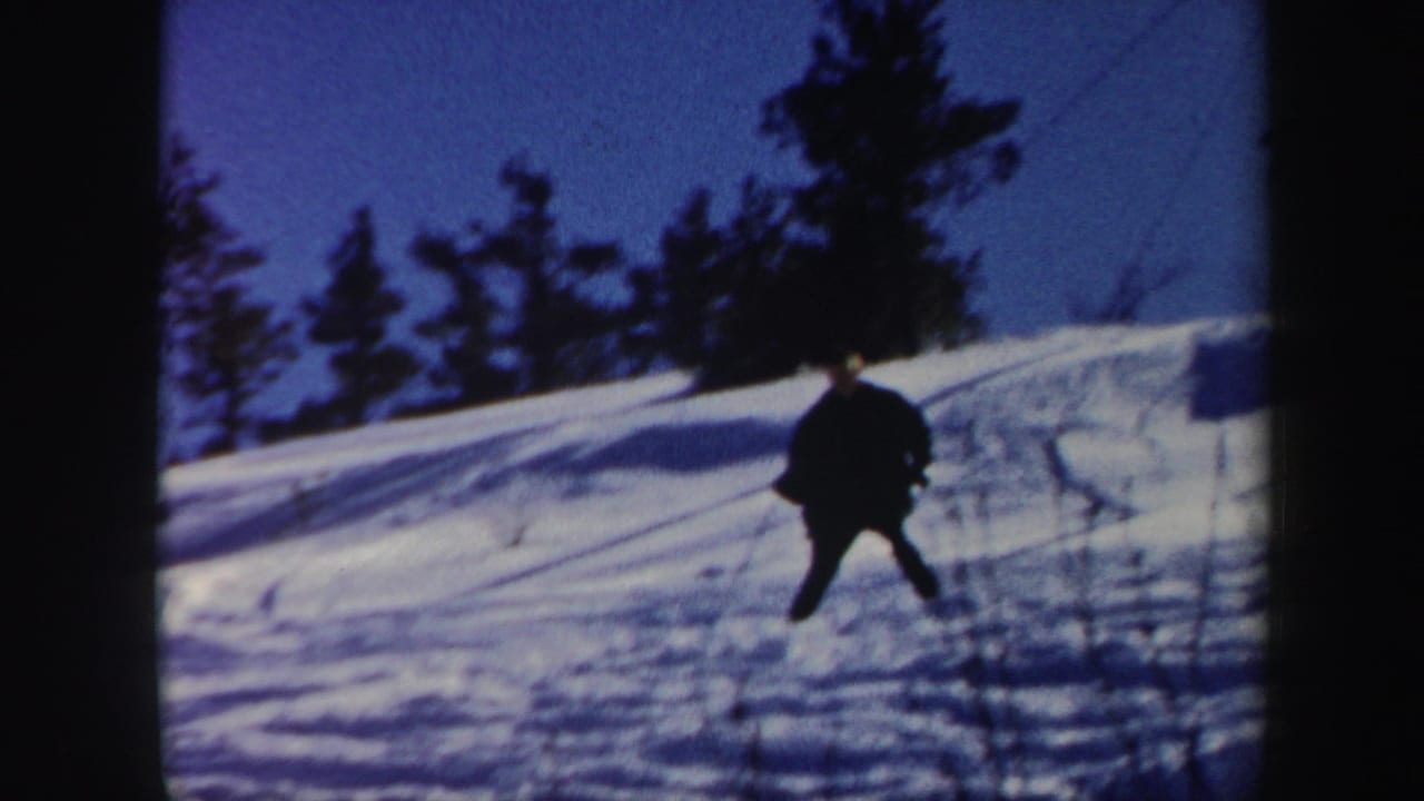 1962 Vermont 8mm frame showing a skier in dark winter clothing on a snow-covered hillside beneath a blue sky.