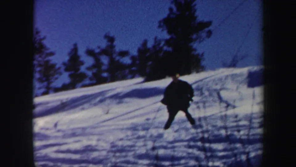 1962 Vermont 8mm frame showing a skier in dark winter clothing on a snow-covered hillside beneath a blue sky.