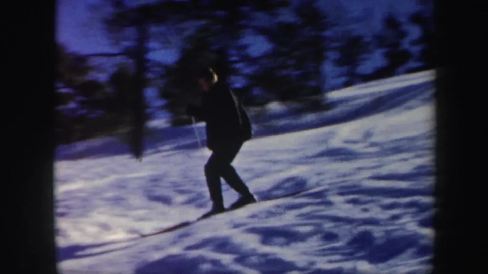 1962 Vermont home-movie frame of a skier traversing a snowy hillside, with dark trees and visible 8mm film borders.