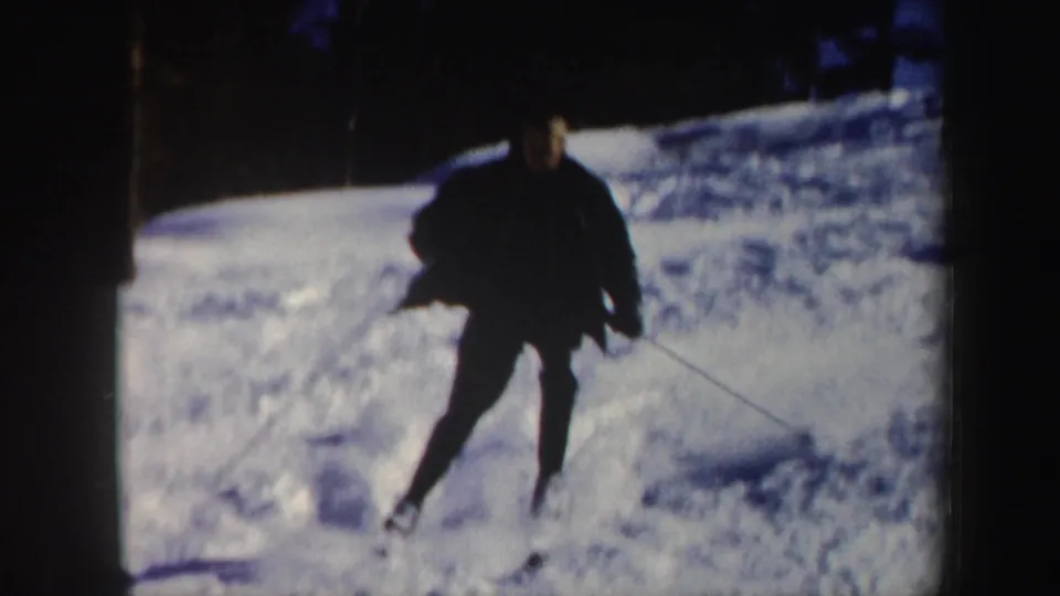 1962 Vermont 8mm frame showing a dark-clad skier coming closer to the camera through bright snow and shadow.