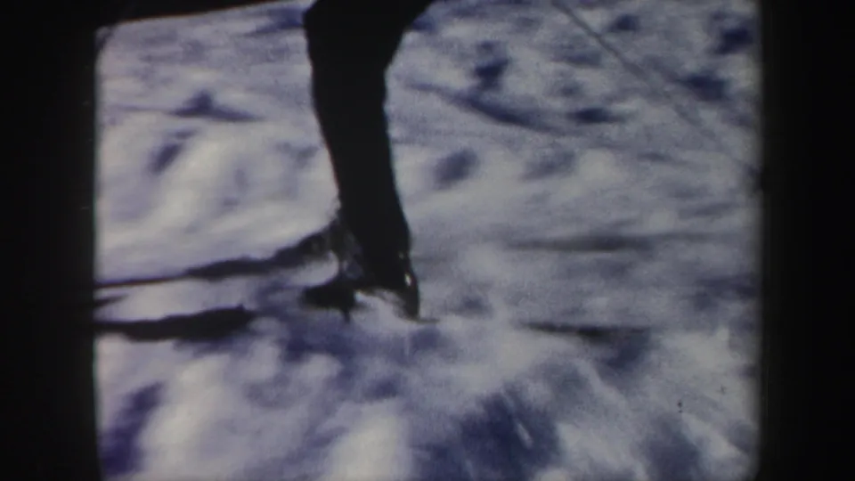 Close 1962 Vermont home-movie frame of a skier's legs and skis passing over textured snow, with strong blur from motion.