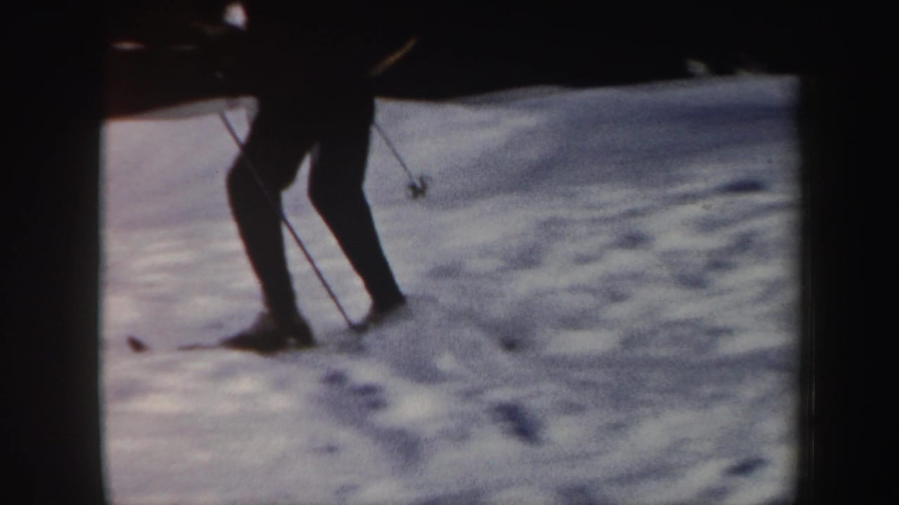 1962 Vermont home-movie frame showing a skier's lower body and poles crossing uneven snow on a resort slope.