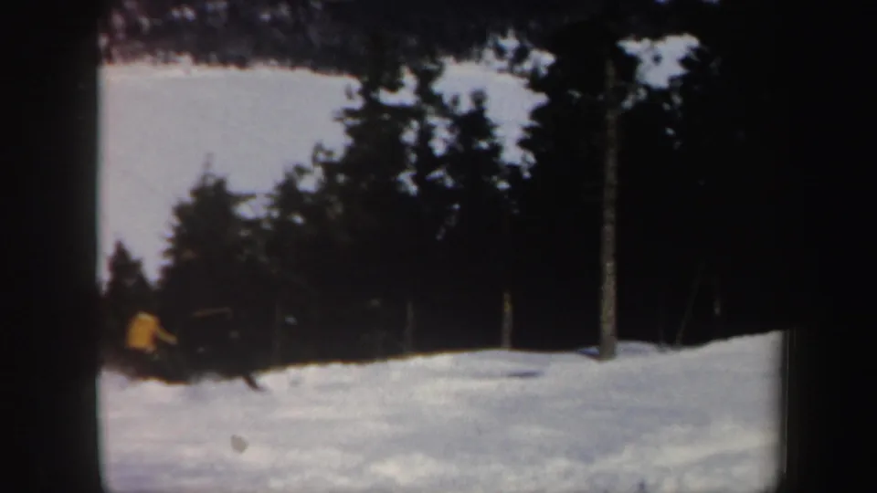 1962 Vermont home-movie frame showing a distant skier on a snowy resort slope near trees and lift infrastructure.