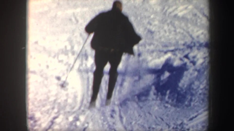 In Vermont 1962 home-movie footage, a skier in a dark coat practices on a snowy slope, filmed from behind with strong glare and grain.