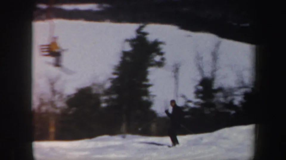 A skier on a Vermont slope is framed with a chairlift rider, evergreens, bare trees, and grainy 8mm exposure in the background.