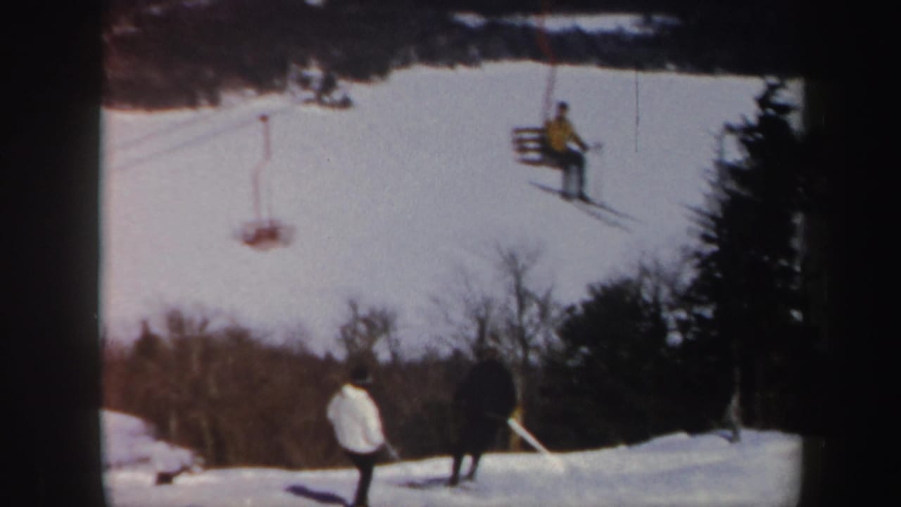 Skiers on a snowy slope with a chairlift passing above.