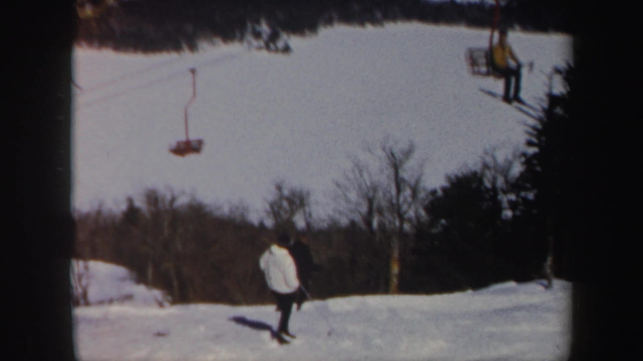 Vermont winter slope with a skier in a light jacket below chairlift equipment and tree-lined snowfields.