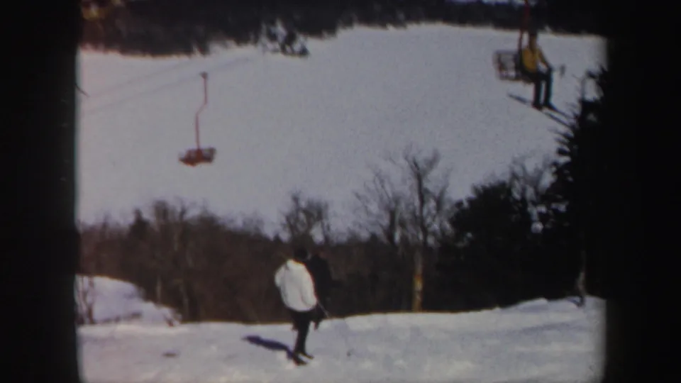 Vermont winter slope with a skier in a light jacket below chairlift equipment and tree-lined snowfields.