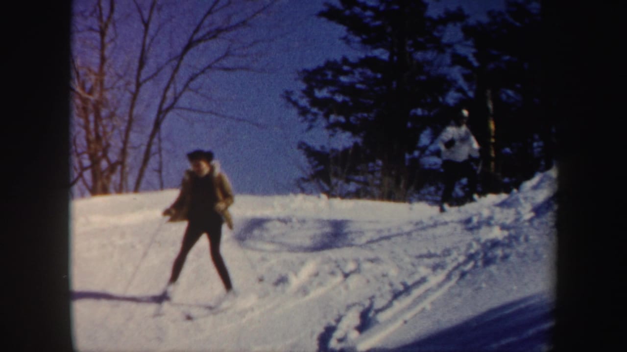 1962 Vermont frame of a skier in dark clothing moving across a bright snowy slope with winter trees behind.