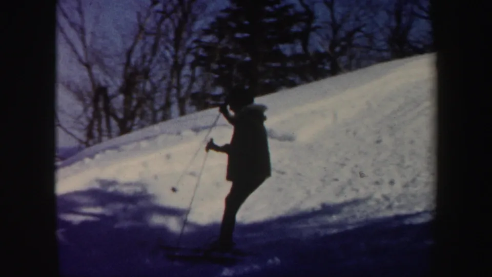 1962 Vermont home-movie frame showing a skier partly silhouetted on a shaded snowbank with trees in the background.