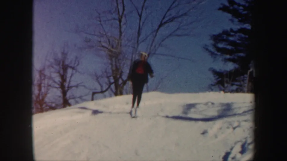 1962 Vermont frame of a skier seen from behind on a snow-covered rise, with winter trees and blue sky beyond.