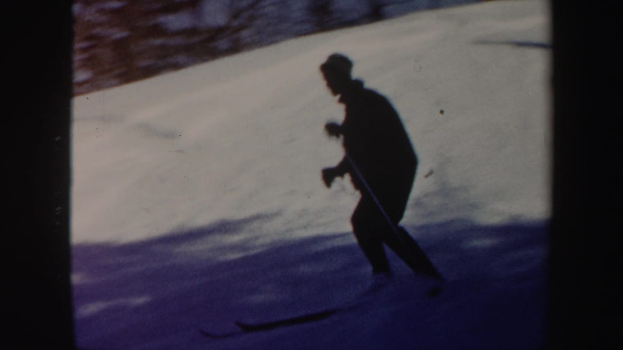 A dark silhouetted skier moves across a bright Vermont snow slope in vintage 8mm winter footage.