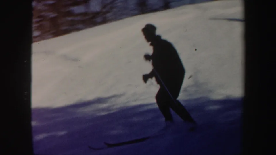A dark silhouetted skier moves across a bright Vermont snow slope in vintage 8mm winter footage.