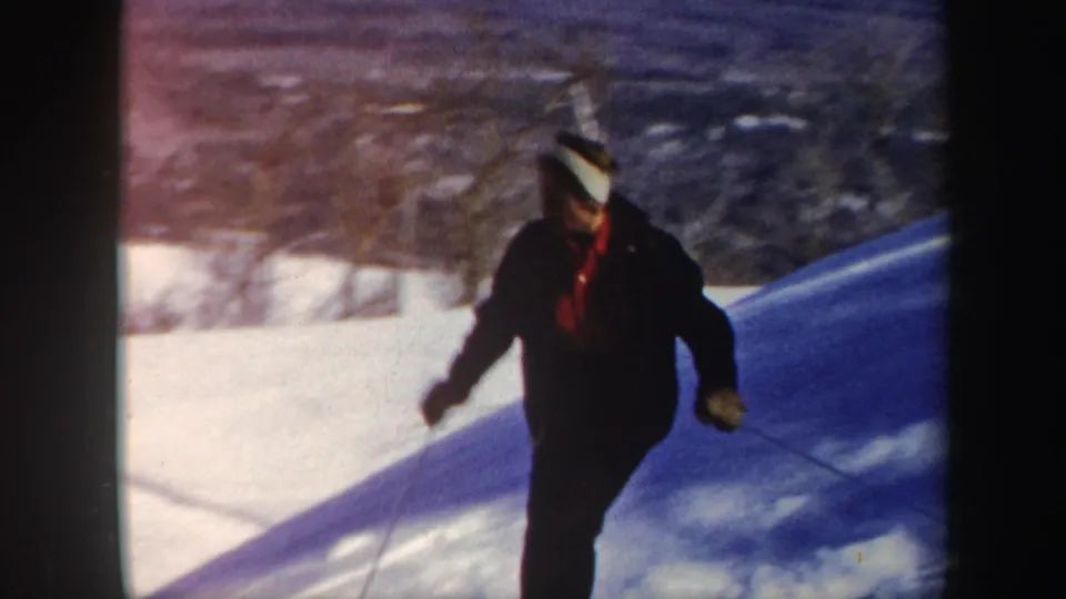 A skier wearing dark outerwear and a red shirt approaches the camera while descending a sunny Vermont hill.