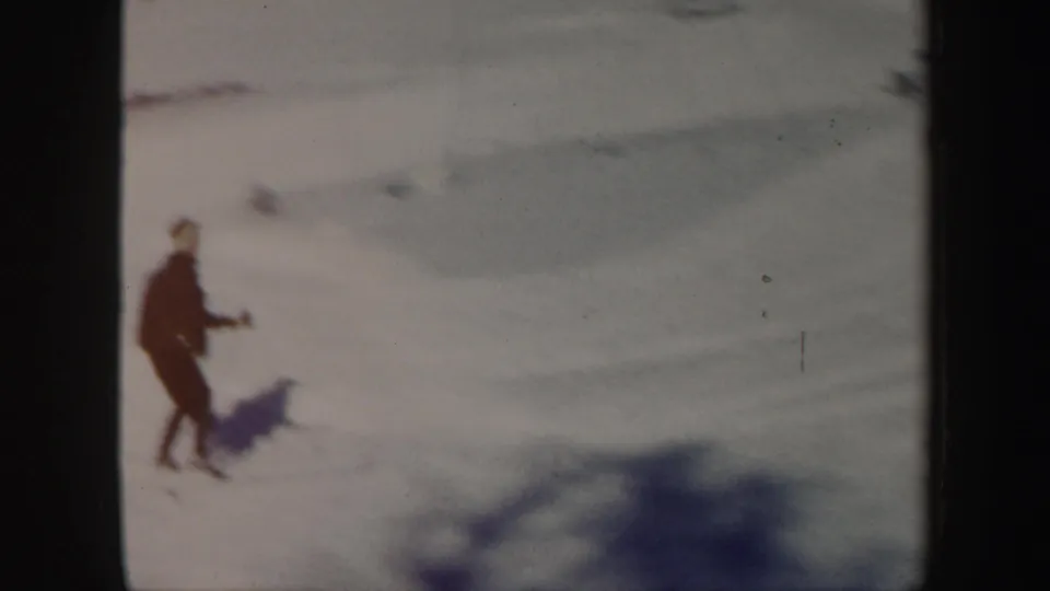 A distant skier in dark clothing moves over bright snow in Vermont winter footage from 1962.