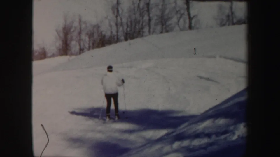A skier in a light jacket appears on a snowy Vermont hillside with bare trees in the background.