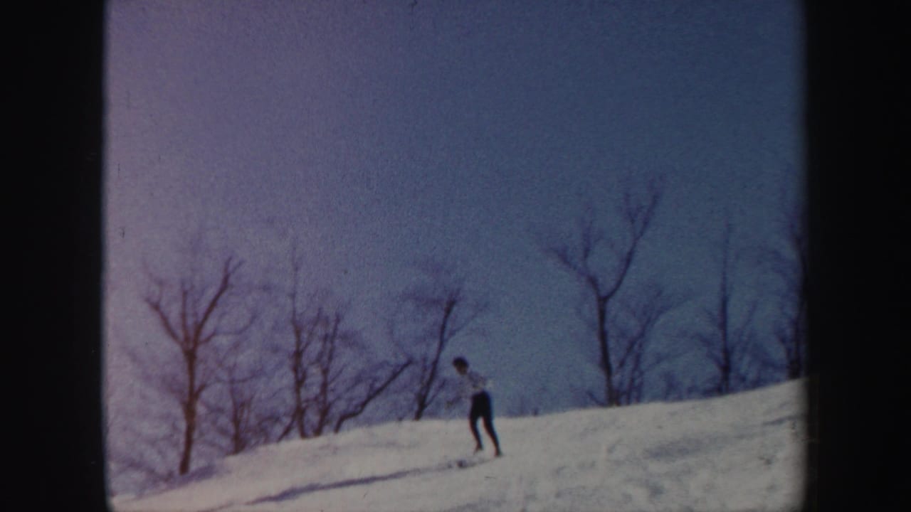 Distant skier descending a snowy ridge under a pale blue sky.