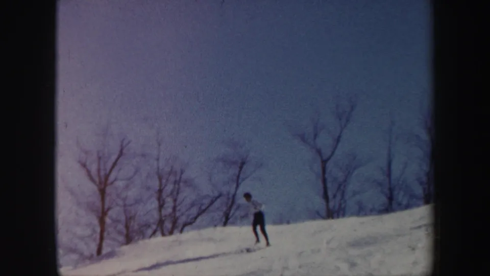 1962 Vermont home-movie frame with a skier on a snow-covered ridge and bare trees silhouetted against the sky.