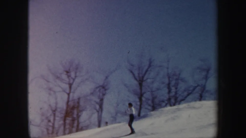1962 Vermont 8mm frame showing a skier moving past leafless trees on a bright snow-covered hill.