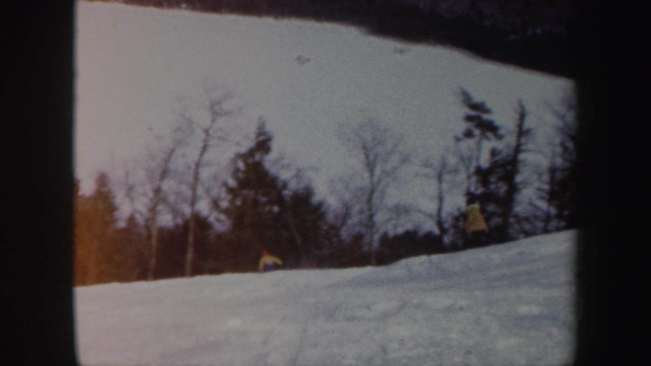 1962 Vermont 8mm frame showing a small skier on a snowy hillside bordered by bare trees and evergreens.