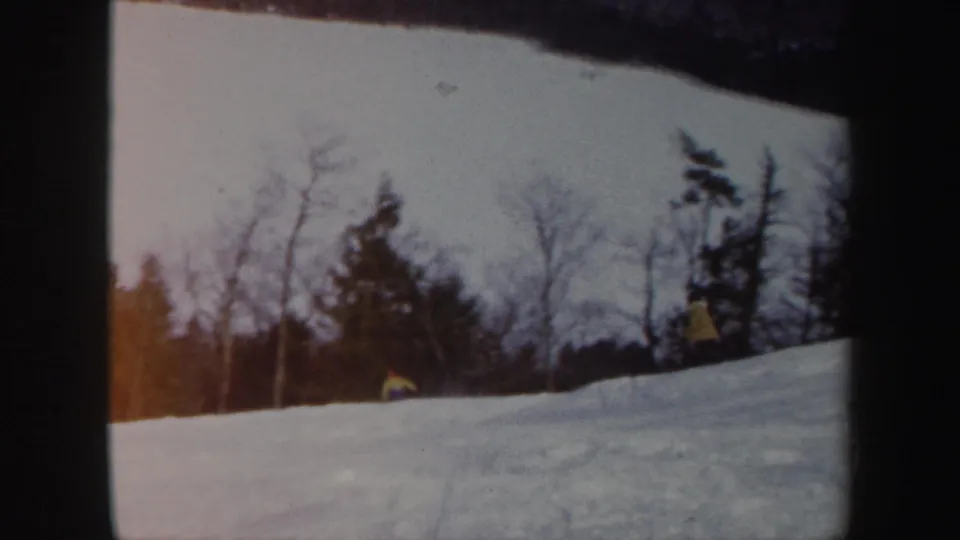 1962 Vermont 8mm frame showing a small skier on a snowy hillside bordered by bare trees and evergreens.
