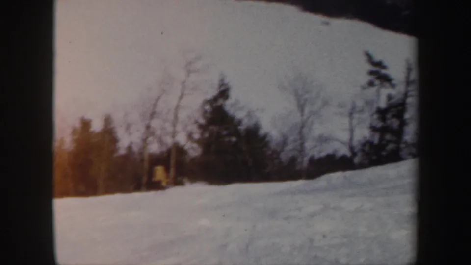 Soft 8mm frame of the yellow-jacketed skier continuing down a snowy Vermont hillside with trees at the top.
