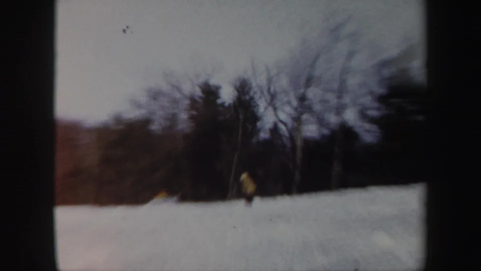 The skier reaches the lower part of the snowy Vermont slope, framed by dark trees and soft home-movie blur.