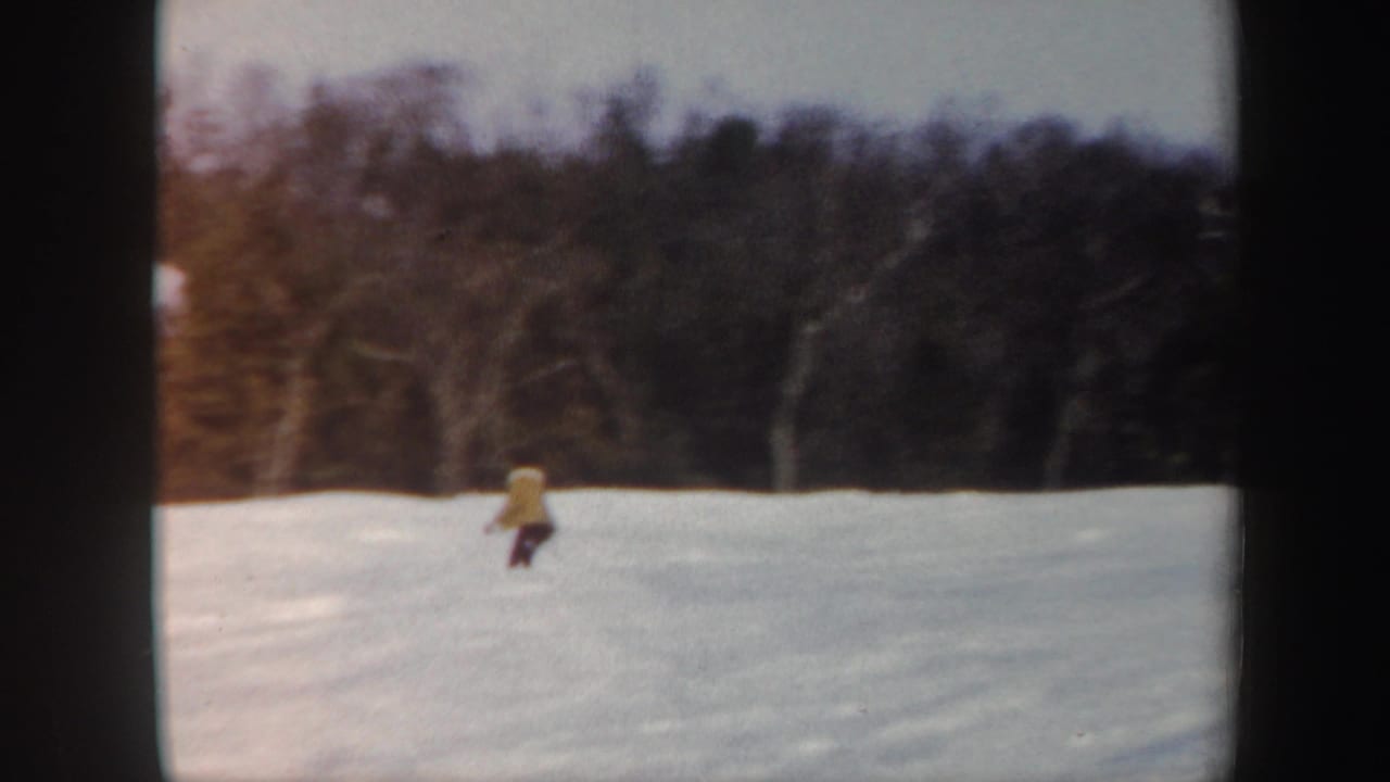 Distant skier in yellow descending an open snow-covered slope.