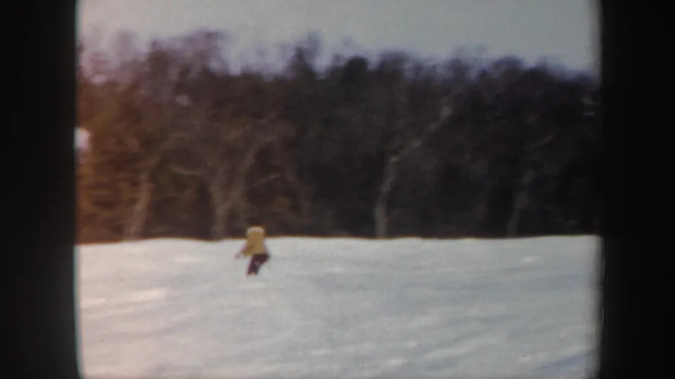 A lone skier in yellow appears mid-slope in the Vermont winter landscape, framed by snow and leafless trees.