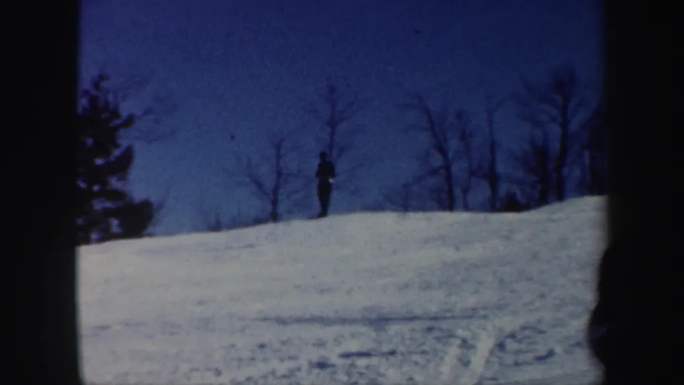 Distant skier silhouetted near the ridge of a Vermont snow slope in soft 1962 home-movie footage.